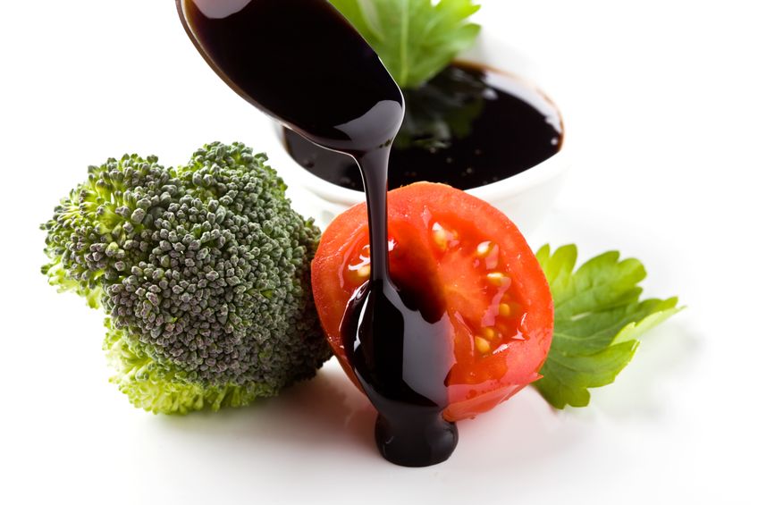 Balsamic vinegar being poured on tomatoes and broccoli